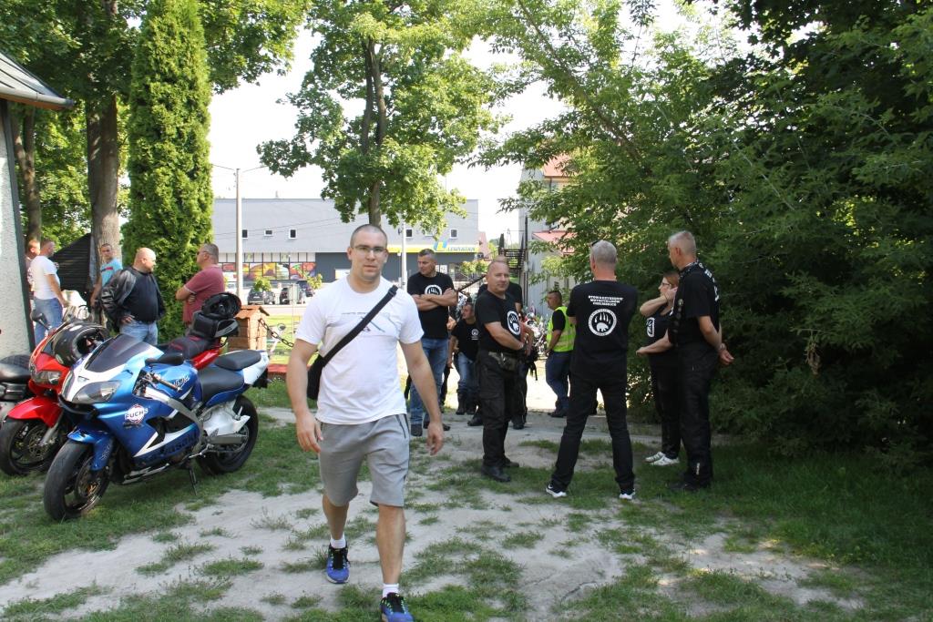 Motocykliści w czarnych koszulkach, obok motocykle. Na pierwszym planie mężczyzna w jasnej koszulce.