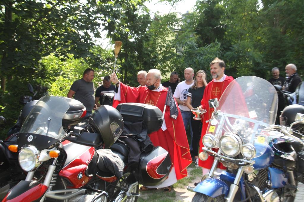 Ksiądz w czerwonej sutannie dokonuje poświęcenia motocykli stojących na dworze