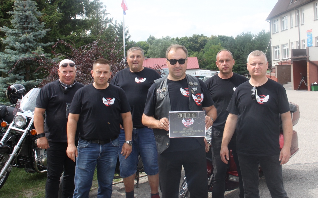 6 motocyklistów w czarnych koszulkach z logo klubu motocyklowego trzyma dyplom