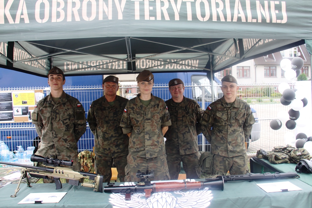 Żołnierze z WOT na stoisku podczas dożynek, żołnierze w postawie stojącej przed nimi na stole broń
